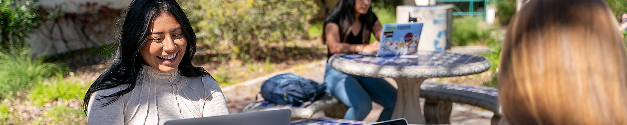 student outside, smiling and working on laptop